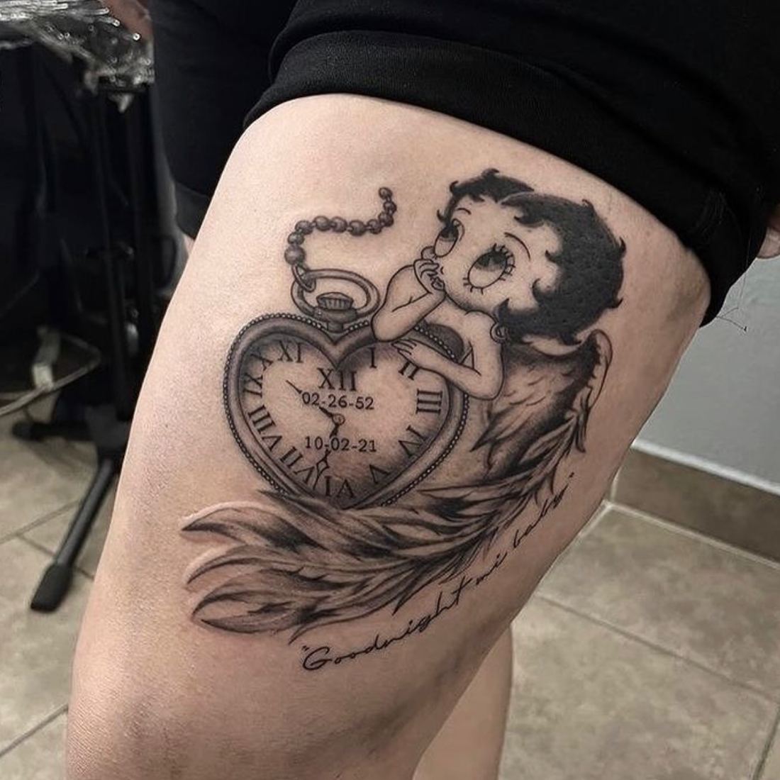 Tattoo of a pocket watch heart with Roman numerals, dates, wings and a cartoon character