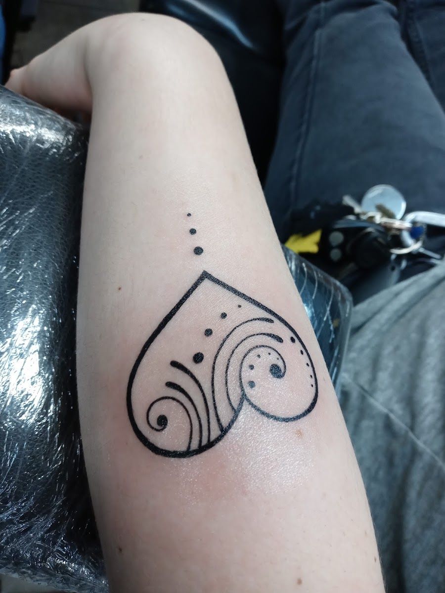 Fine line heart tattoo with swirls and dots on a forearm