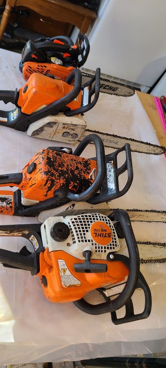 Three orange chainsaws lined up on a bench