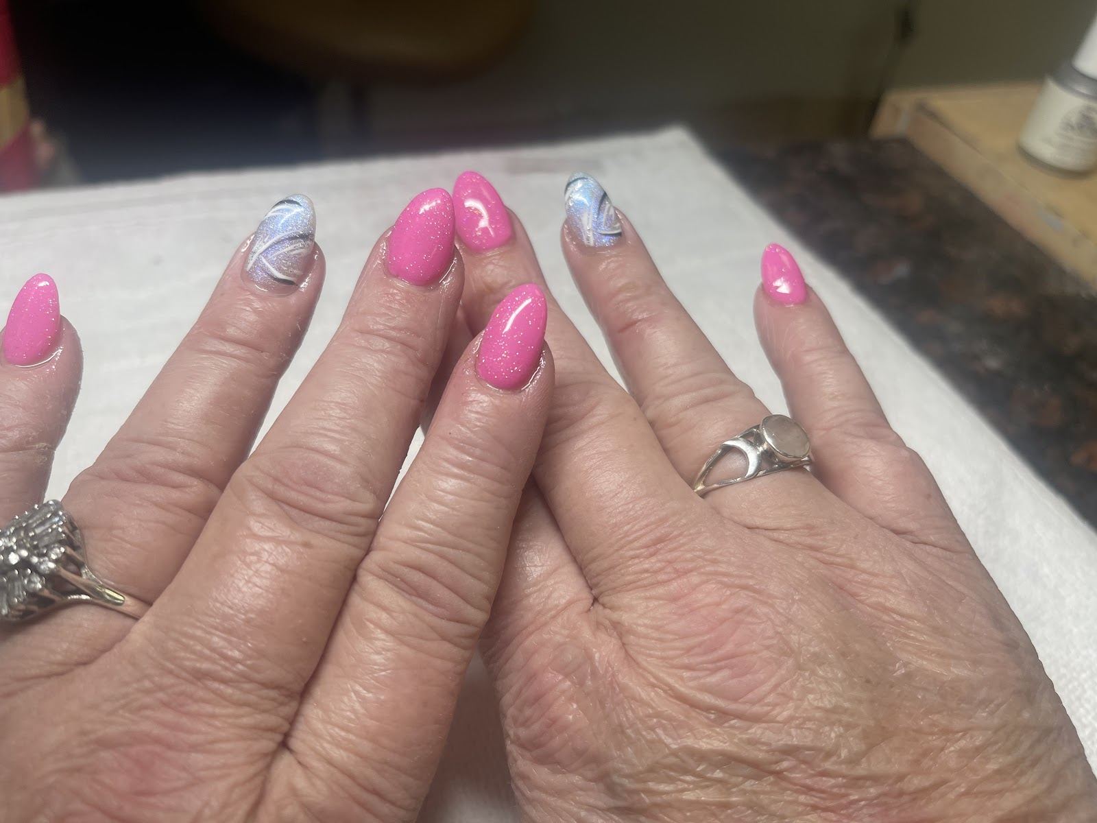 Hot pink almond gel nails with glitter, and two silver-white swirl accent nails