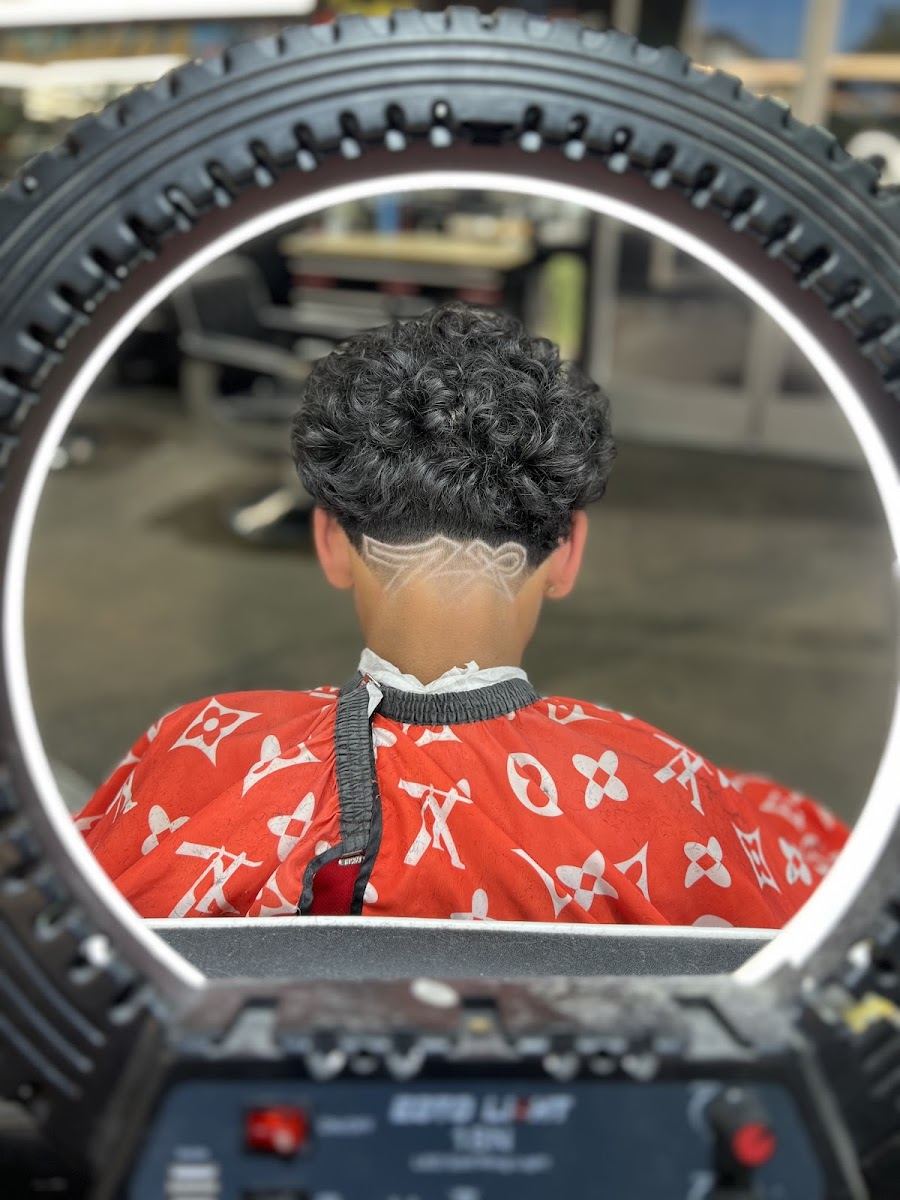 Curly top with a freestyle design shaved into the nape, framed by a ring light