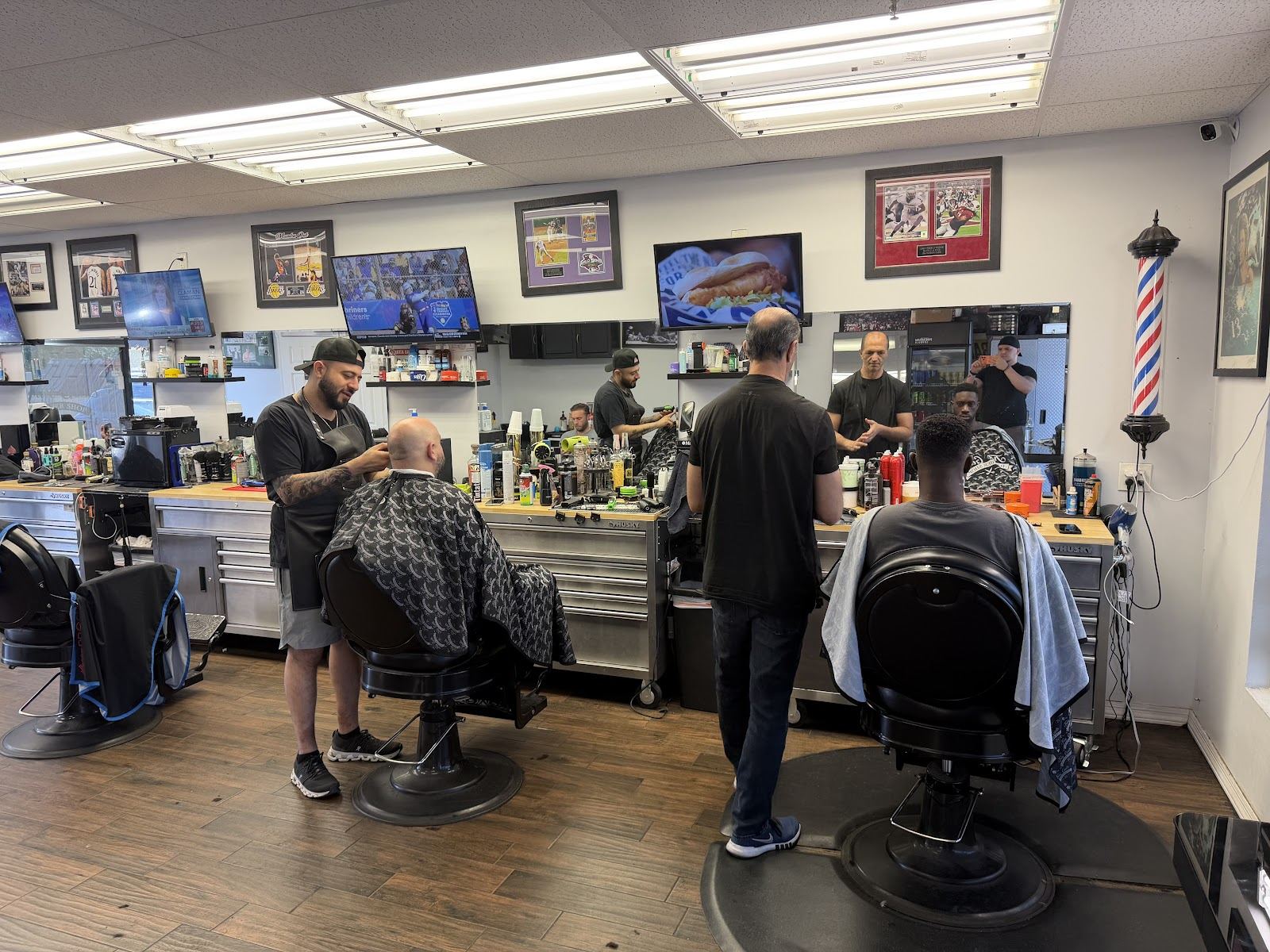 Barbers at work inside True Gents Barbershop, with framed art and a barber pole on the wall