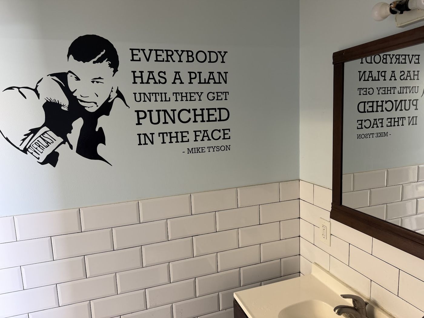 Wall art with a boxing quote above white subway tile