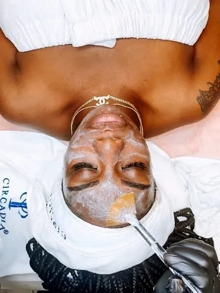 A client lying back with a treatment mask on her face and a soft towel wrap on her hair