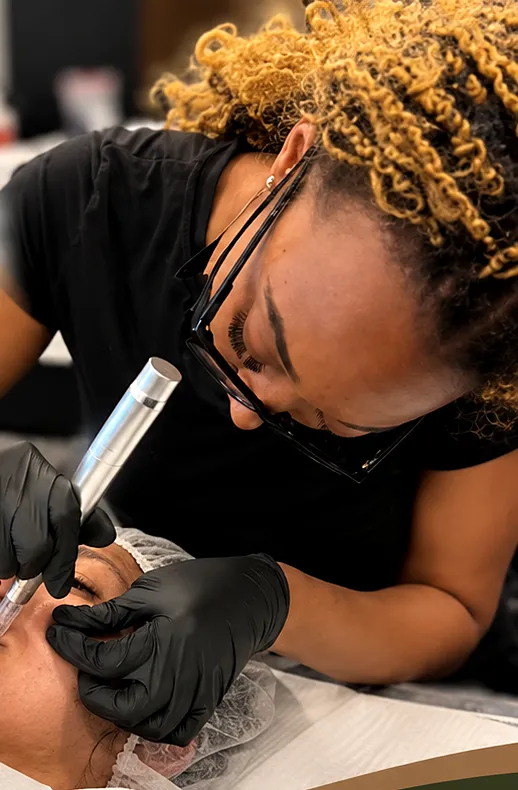 Raven in glasses and black gloves running a microneedling pen across a client's cheek