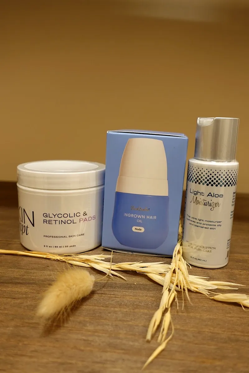 Three skincare products on a wooden counter beside dried wheat stems