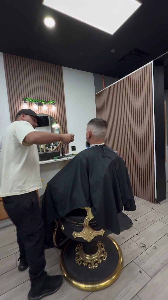 A barber cleaning up a client's fade in a black and gold chair