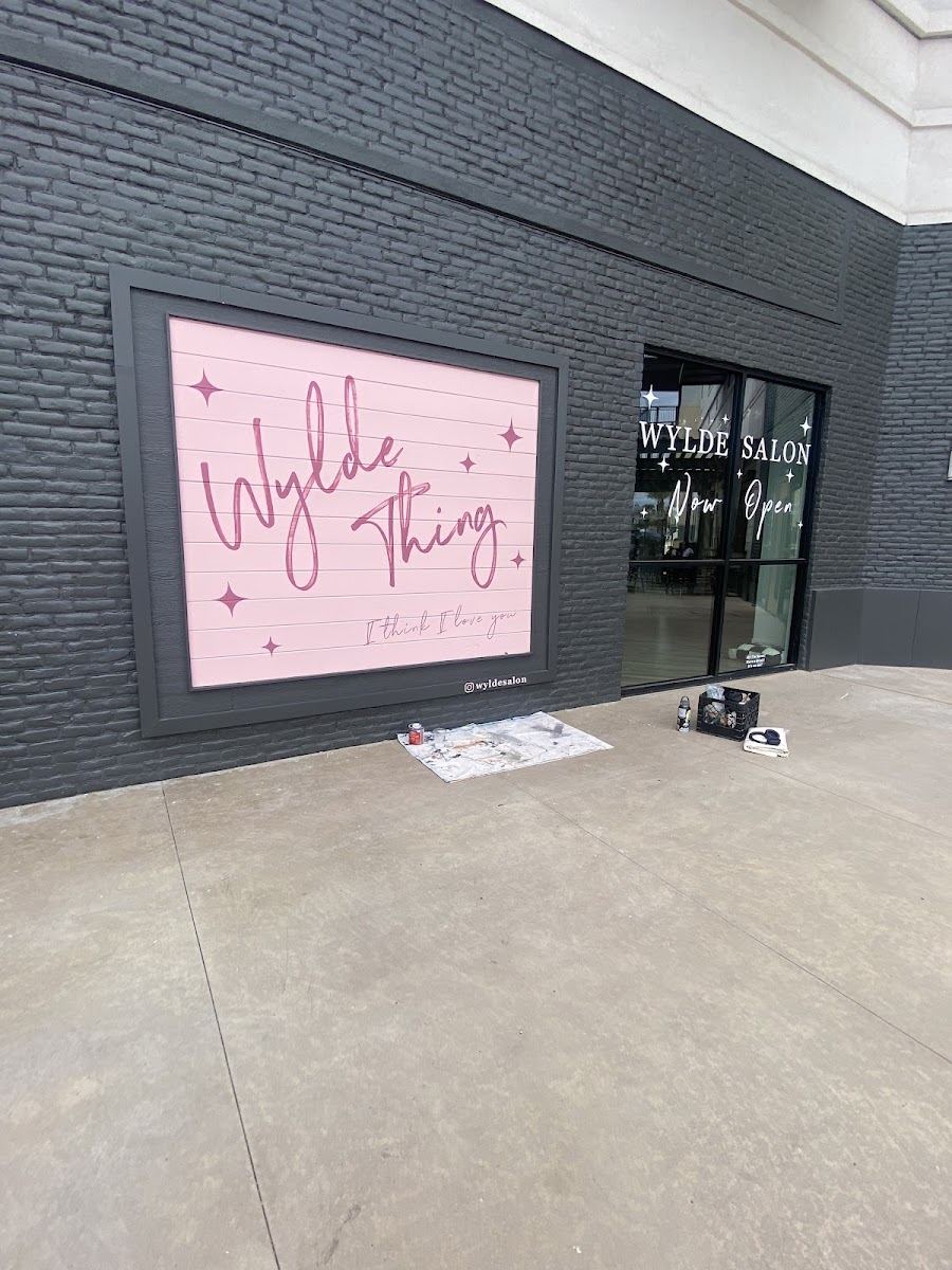 The pink Wylde Thing mural on the dark brick wall outside the salon